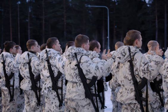 Alokkaat vannomassa valaa muodossa selin kameraan. Päällään heillä on lumitakki ja -housut sekä selässä ase.