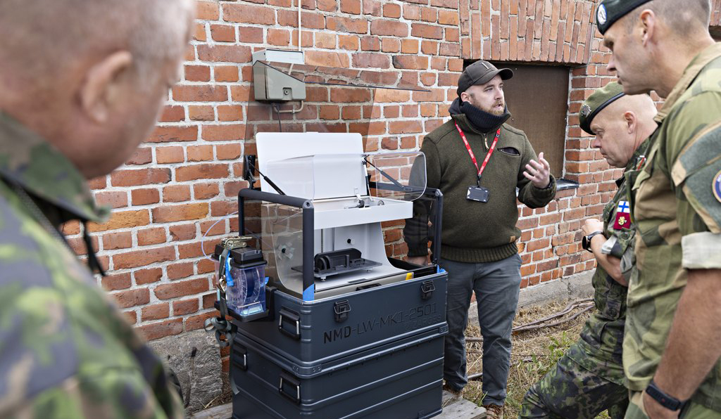 På bilden bekantar sig fyra män – tre soldater och en civil – med en 3D-skrivare.