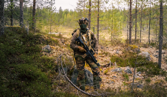 A French soldier standing in the woods in full combat gear.