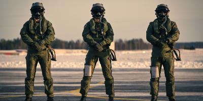 Kolme lentovarusteisiin pukeutunutta henkilöä seisoo rivissä rintamasuunta kameraan päin. Kuva on otettu lentokentän alueella talvella, ja lentokypärien visiirit ovat alhaalla.